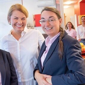 Drei freundliche Zahnärztinnen und ihr Praxisteam begrüßen Patienten in moderner Zahnarztpraxis.