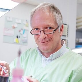 Zahntechniker arbeitet konzentriert im Labor an Zahnersatz unter hellem Licht.