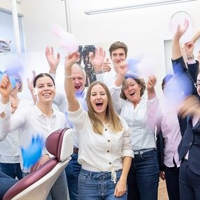 Fröhliches Zahnarztpraxis-Team feiert gemeinsam in moderner, heller Praxisumgebung.